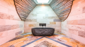 A luxurious bathroom with a freestanding stone bathtub, a textured stone wall, and a skylight.