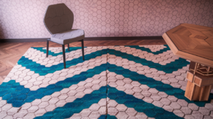 A modern interior design featuring a unique geometric rug with a blue and beige pattern, a statement chair, and a wooden table.