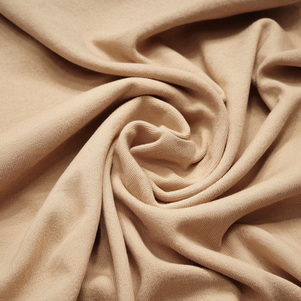  A beige modal fabric swatch elegantly folded, placed on a rustic wooden surface, with a book titled "The Ultimate Guide to Modal Fabric" featuring a green leaf on the cover in the background.